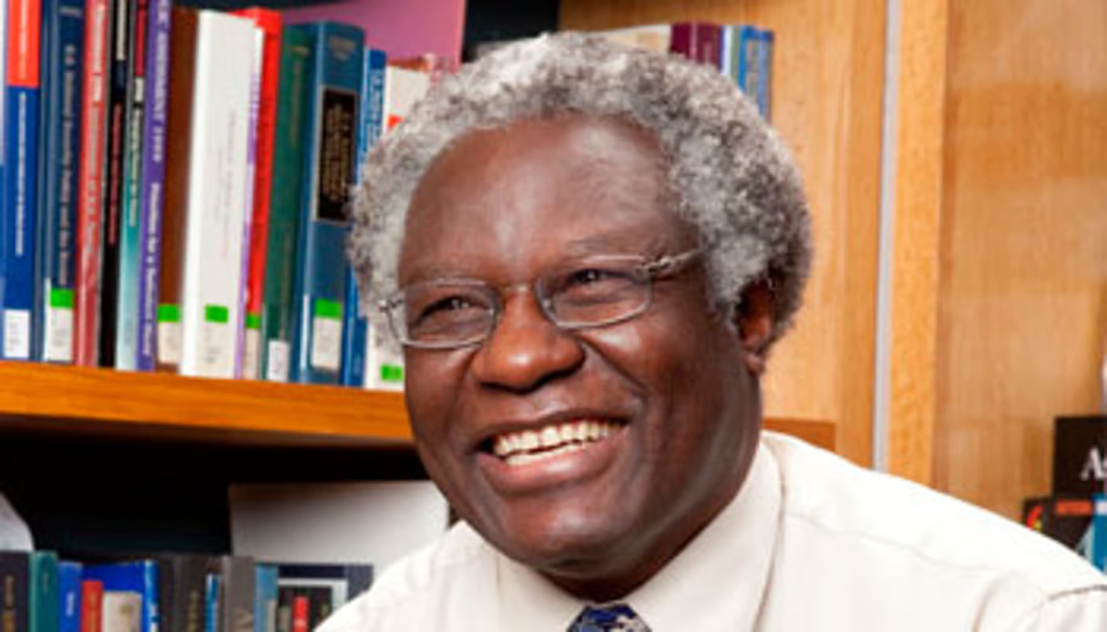 Calestous Juma laughs in front of a bookshelf